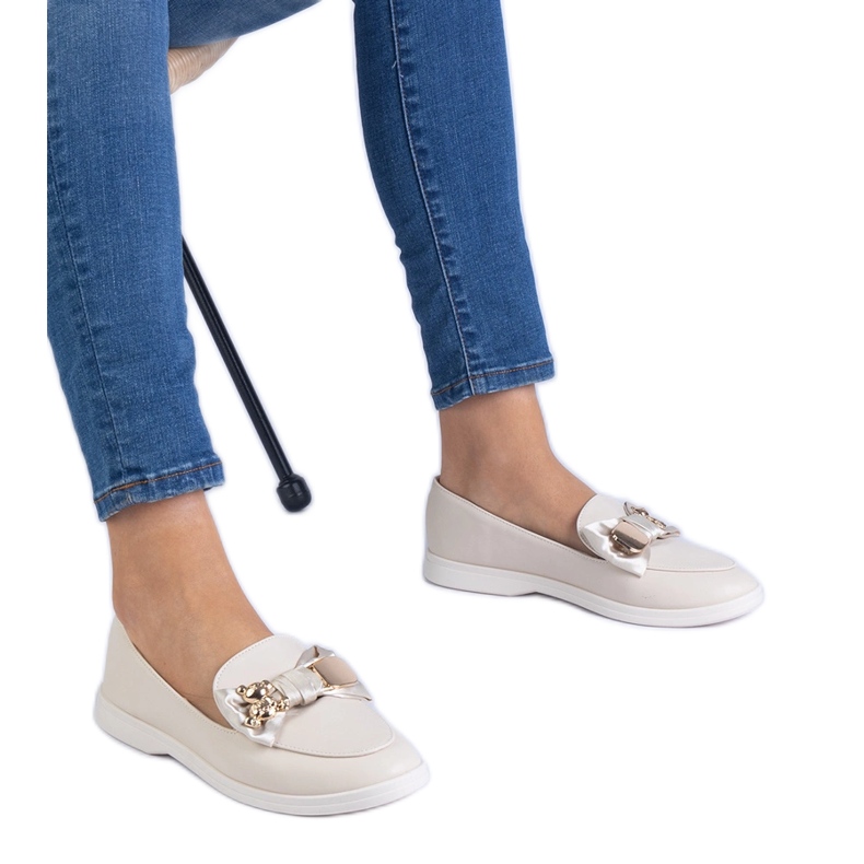 Beige loafers dekorerade med en båge och en gyllene nallebjörn