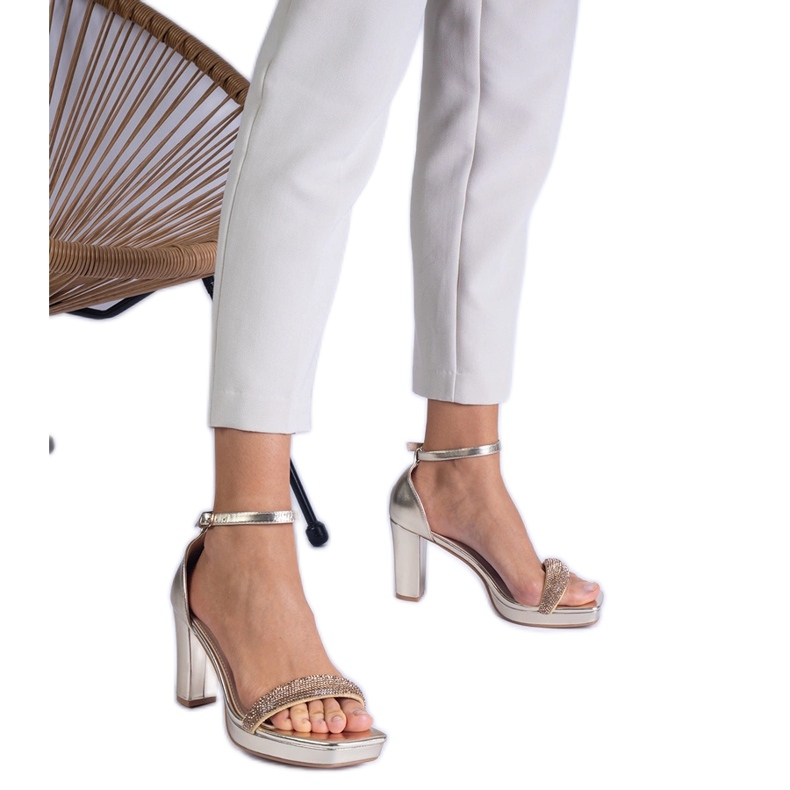 Gyllene eleganta sandaler på pelaren med zirkoner