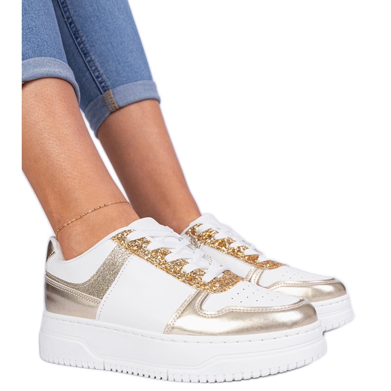 Gyllene kvinnors sneakers på en tjock sula dekorerad med glitter